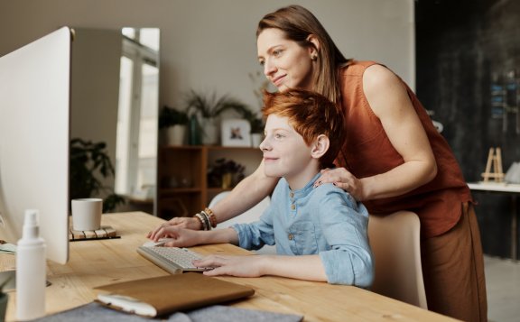 a parent looks at the computer screen with child over the shoulder