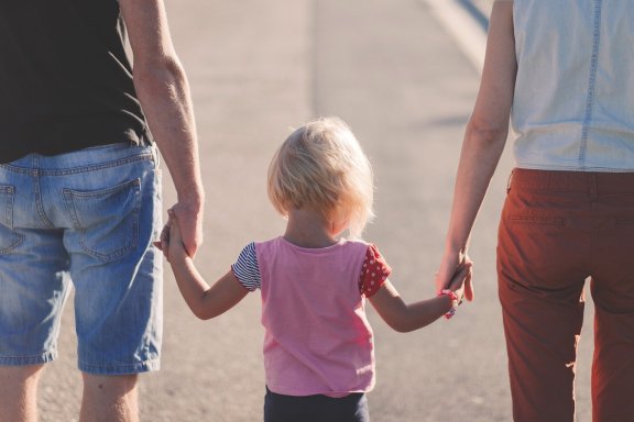 child holds hands with two adults