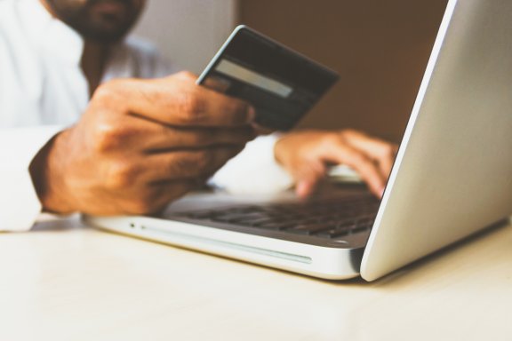 man shops online at laptop with credit card in hand